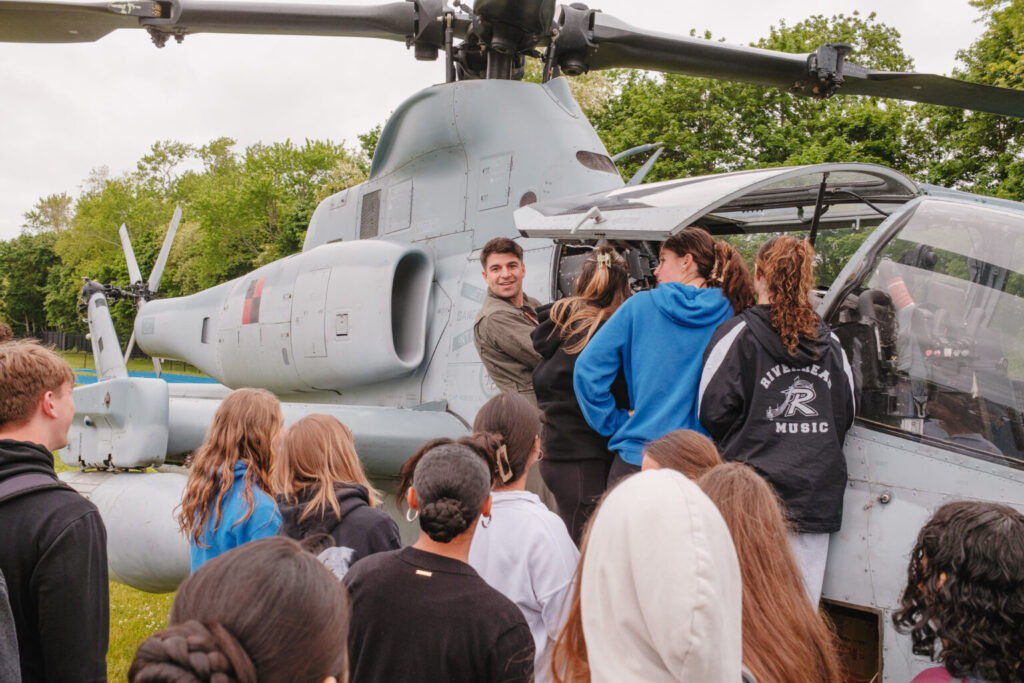 A group of students stand outside a military helicopter