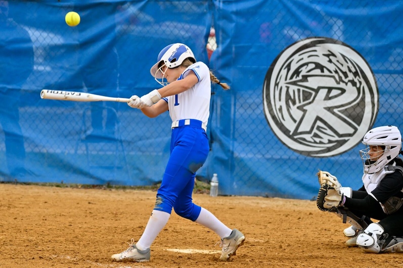 A Blue Waves softball player swings and hits.