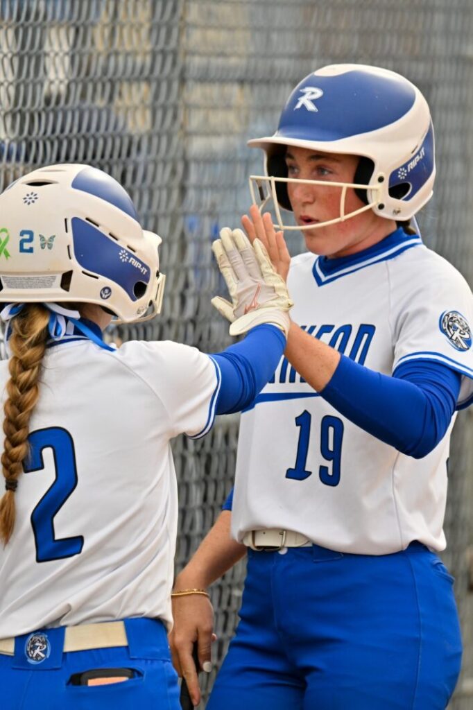 Two Blue Waves softball players high five after scoring.