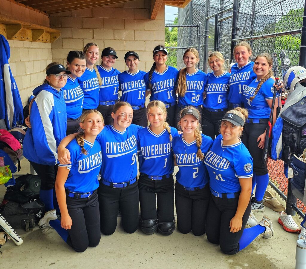 The Riverhead softball team lines up in two lines, one of girls in blue jerseys standing and one row kneeling in front.