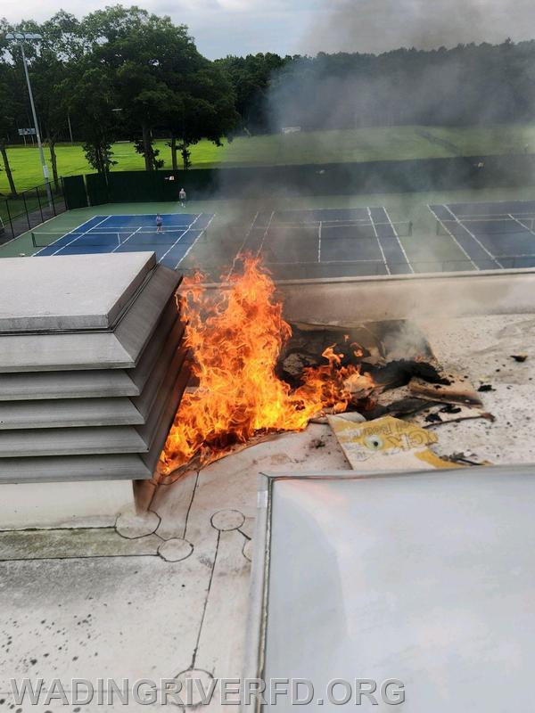 A small fire blazing and smoking atop a school's building.