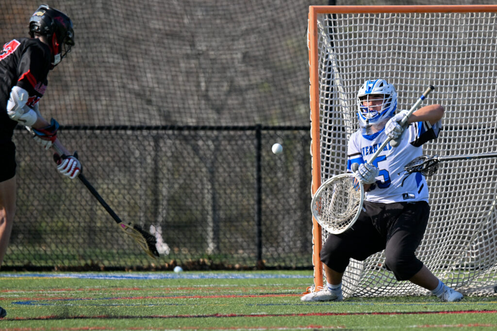 A lacrosse goalkeeper readies himself to catch the ball after the opponent's shot.