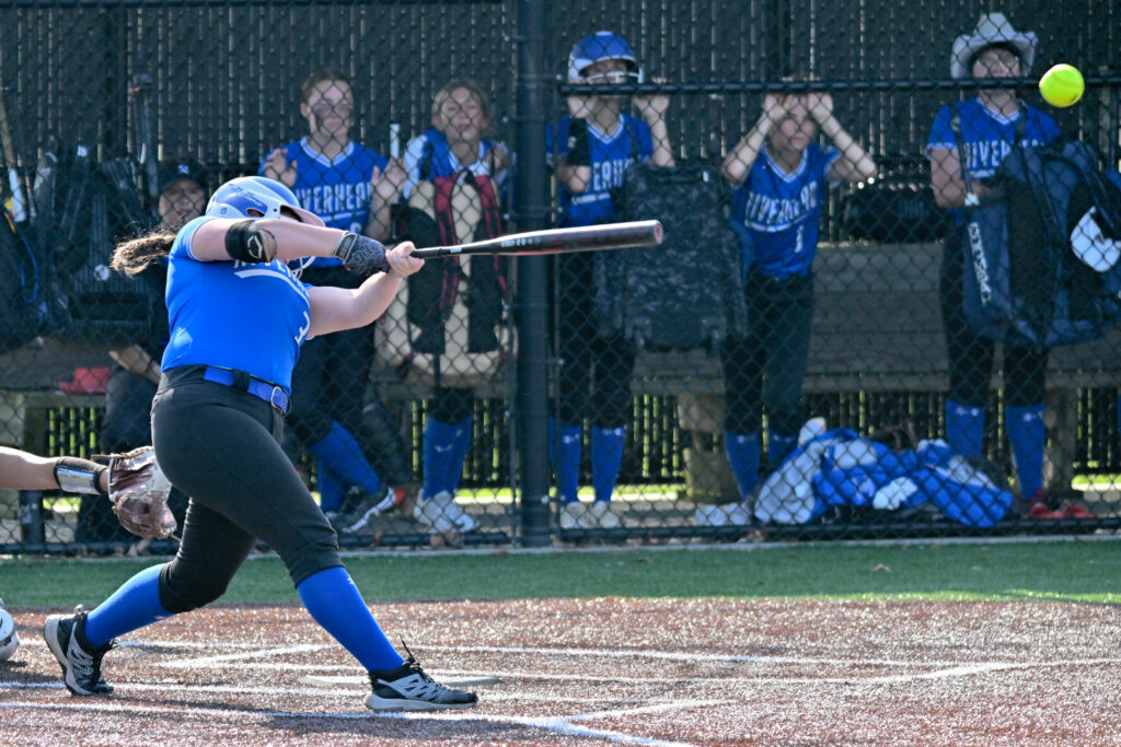 A highschool softball player in a blue jersey with black pants and blue socks hits a yellow softball