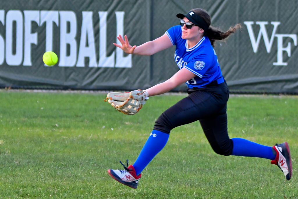 A softball player in a blue jersey, black pants and blue socks catches the ball.